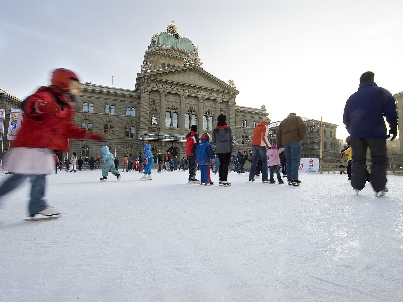 Das Foto zeigt Kinder und Erwachsene, die auf dem Bundesplatz Schlittschuh laufen. Im Hintergrund ist das Bundeshaus zu sehen. 